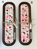 Two rectangular wooden trays containing white wax with embedded pink and purple dried flowers, tied with twine and labeled 'poisoning resistance' on a white background.