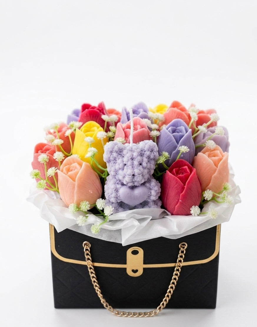 Colorful flower arrangement with a teddy bear inside a black handbag on a white background