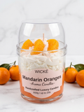 A clear glass jar candle with a clear dome lid, filled with white wax and topped with orange mandarin slices. The front label reads 'WICKÉ Mandarin Oranges'.
