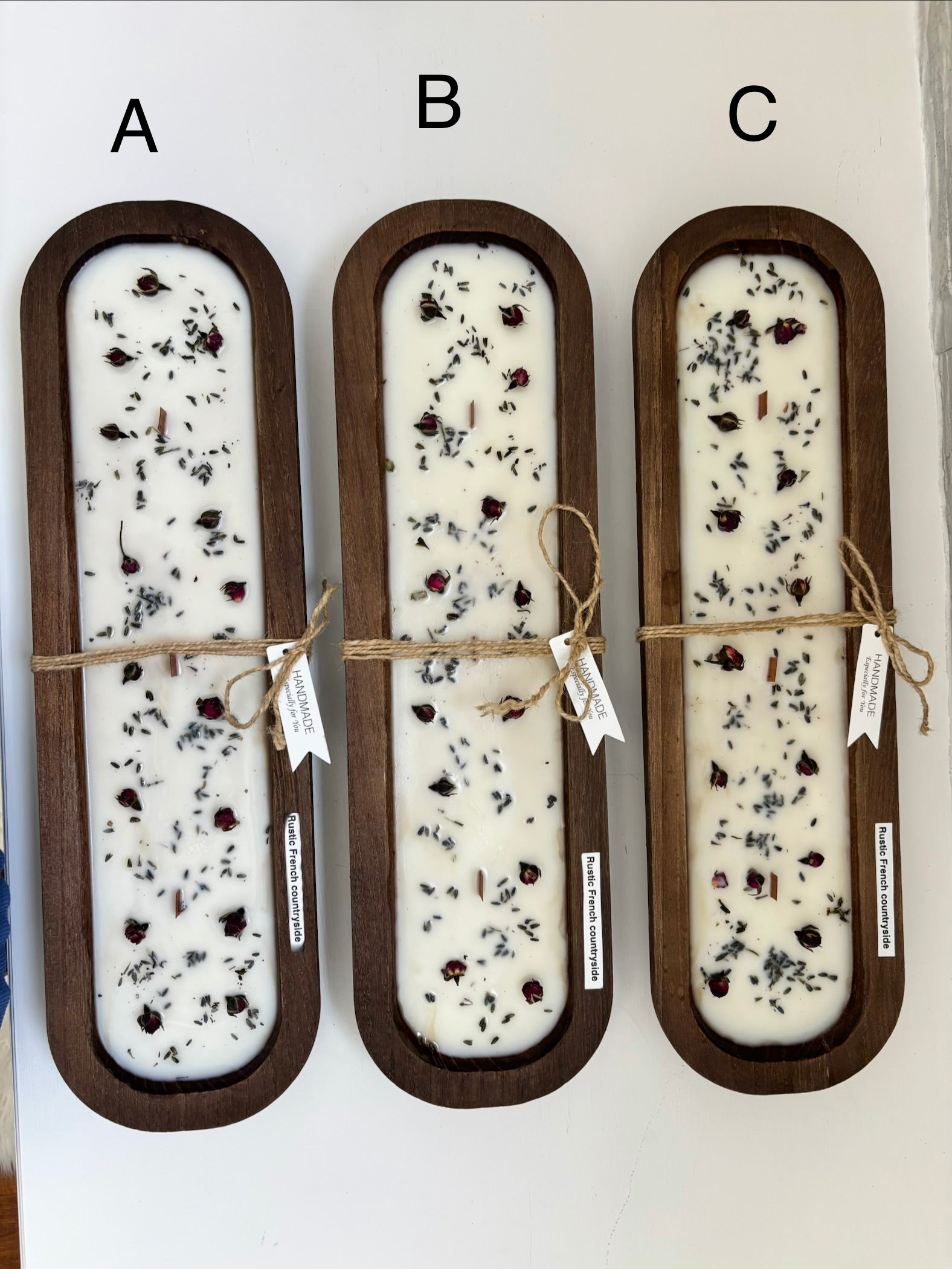 Three rectangular wooden CANDLES labeled A, B, and C, each filled with white soap and dried botanicals, tied with twine and shown against a plain white background.