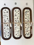Three rectangular wooden CANDLES labeled A, B, and C, each filled with white soap and dried botanicals, tied with twine and shown against a plain white background.