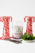 A WICKÉ 'Candy Cane' scented candle in a clear glass jar with a clear plastic dome lid, featuring white wax topped with candy cane and peppermint decorations, and a pink label on a white background.