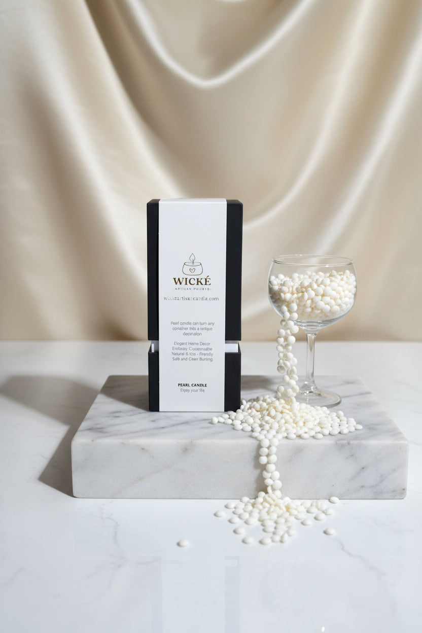 A dramatic, high-fashion editorial studio shot. The WICKÉ White Musk box is centered on a polished white marble block with subtle grey veining. A beautiful glass chalice next to it overflows elegantly with loose white wax pearls. The lighting is crisp and cool, casting soft, architectural shadows against a solid, seamless silk-textured cream backdrop. The entire composition screams premium boutique quality.
